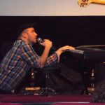 Dueling Hobbits Piano Nick Plaid Kneeling At Piano With Mic